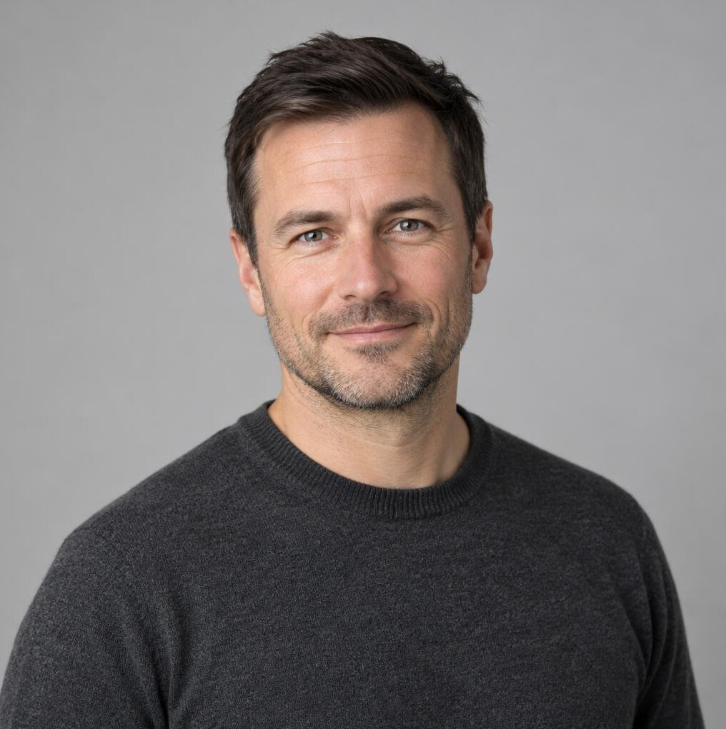 Man with short dark hair and light stubble in a studio portrait